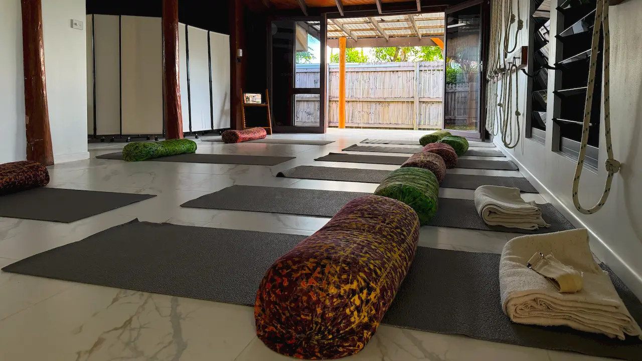 The Kewarra Beach studio set up before class, with mats, bolsters and folded blankets on the floor and the doors open to the garden